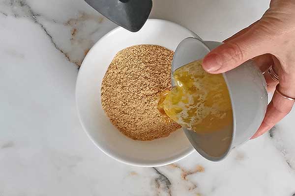 dodawanie rozpuszczonego masła do pokruszonych herbatników, aby zrobić z nich spód do sernika z nutellą
