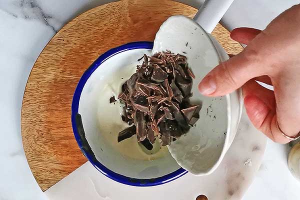 dodawanie posiekanej czekolady do gorącej śmietany kremówki, aby zrobić polewę czekoladową