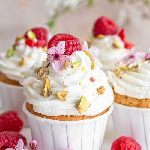 a group of cupcakes with white frosting and raspberries