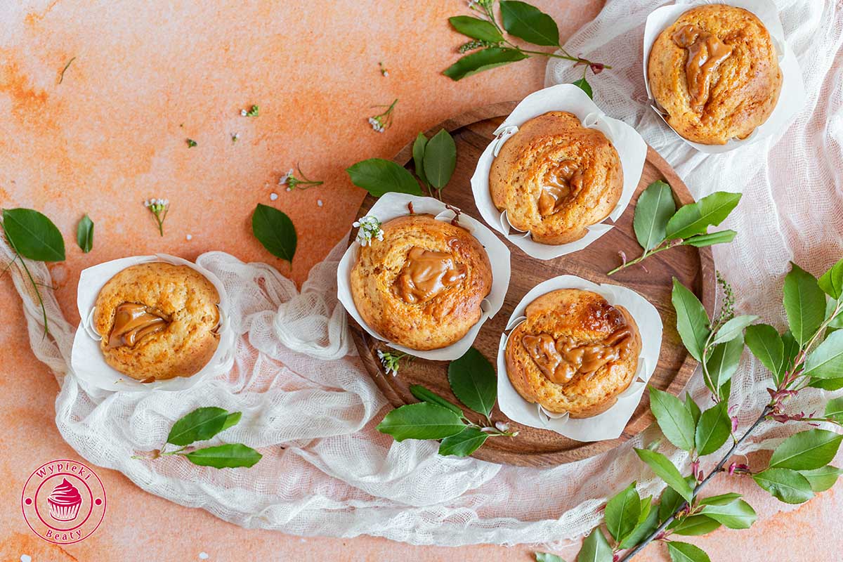 proste babeczki z masą kajmakową widok na 5 z nich ułożonych na gazie proste i szybkie muffiny kajmakowe ułożone na pomarańczowym tle i sfotografowane od góry