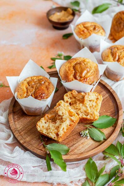 trzy muffiny kajmakowe na talerzu drewnianym, jedna z nich jest przedzielona na pół i odwinięta z papierka