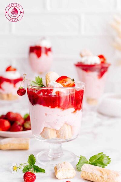 simple strawberry pudding dessert in a glass zbliżenie na szklaneczkę z truskawkowym deserem udekorowanym frużeliną truskawkową oraz świeżymi truskawkami