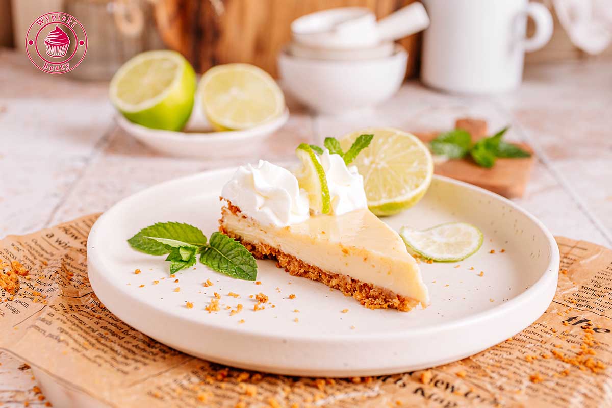 ukrojony kawałek tarty limonkowej na deserowym talerzyku widok od przodu na ukrojony kawałek tarty key lime pie z bitą śmietaną i plasterkiem limonki