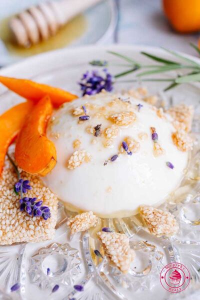 porcja miodowej panna cotty na talerzyku udekorowana miodem, pokruszonymi sezamkami oraz lawendą