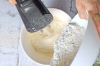 dodawanie przesianej mąki do miski z ciastem