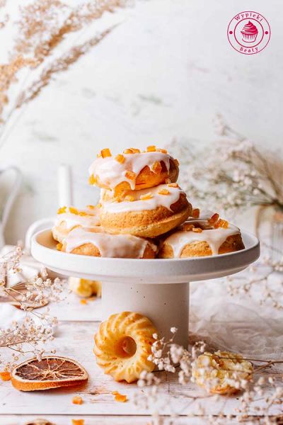 patera z ułożonymi na niej pieczonymi oponkami pomarańczowymi z lukrem i kandyzowaną skórką pomarańczową lekkie i miękkie oponki pieczone z lukrem pomarańczowym