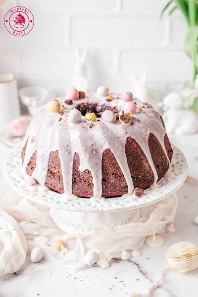 wilgotna i miękka babka wielkanocna z lukrem i czekoladowymi jajeczkami babka na wielkanoc oblana lukrem ułożona na paterze do ciasta